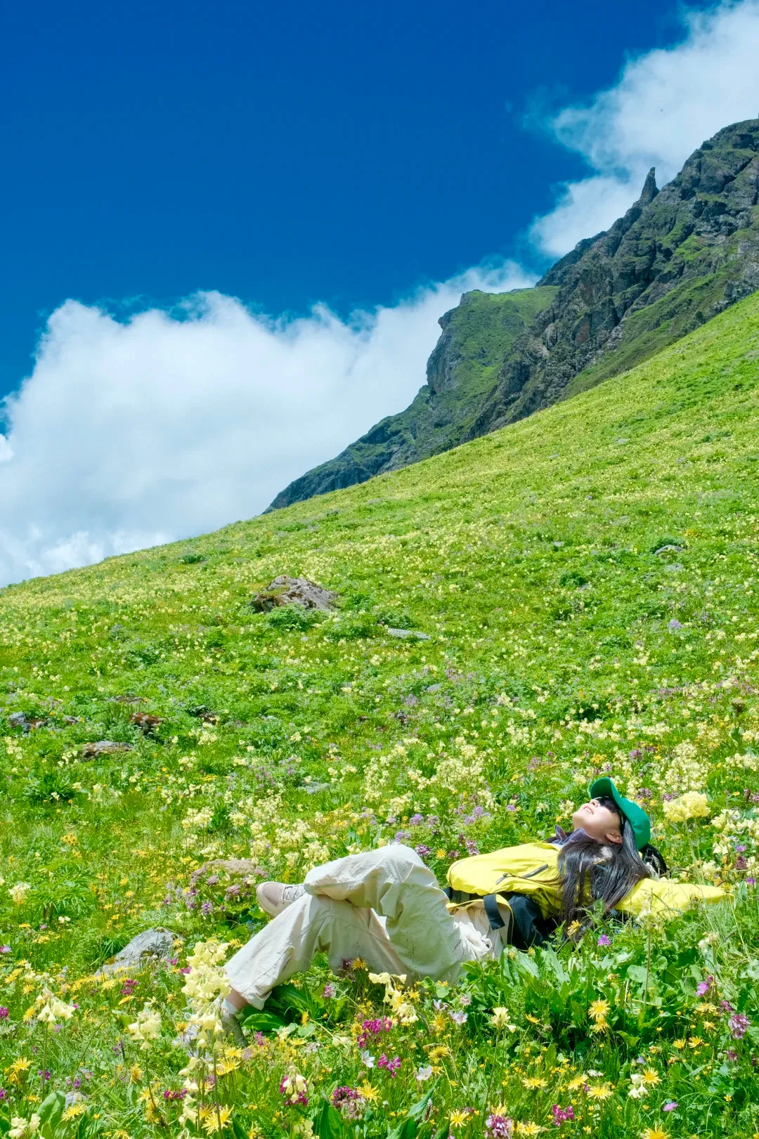 A hiker lying back on a meadow blanketed with pale-yellow primulas, soaking up the sun