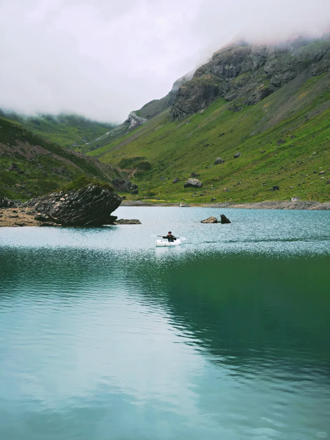 A white packraft floating on the lake's Tiffany-blue-to-jade gradient, tiny against the valley walls