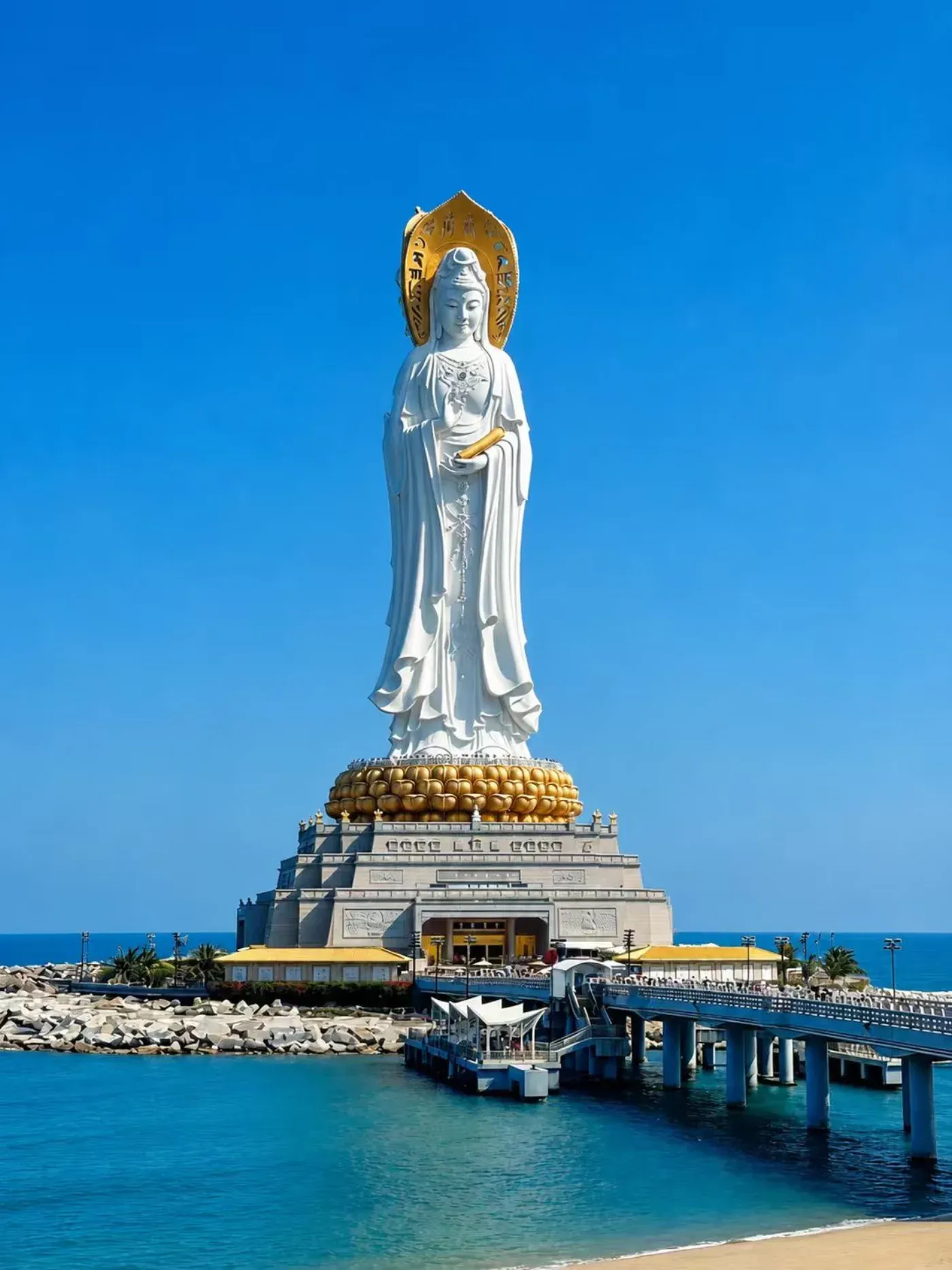 The white Sea Guanyin statue at Nanshan rising above the coastline, seen from across the water
