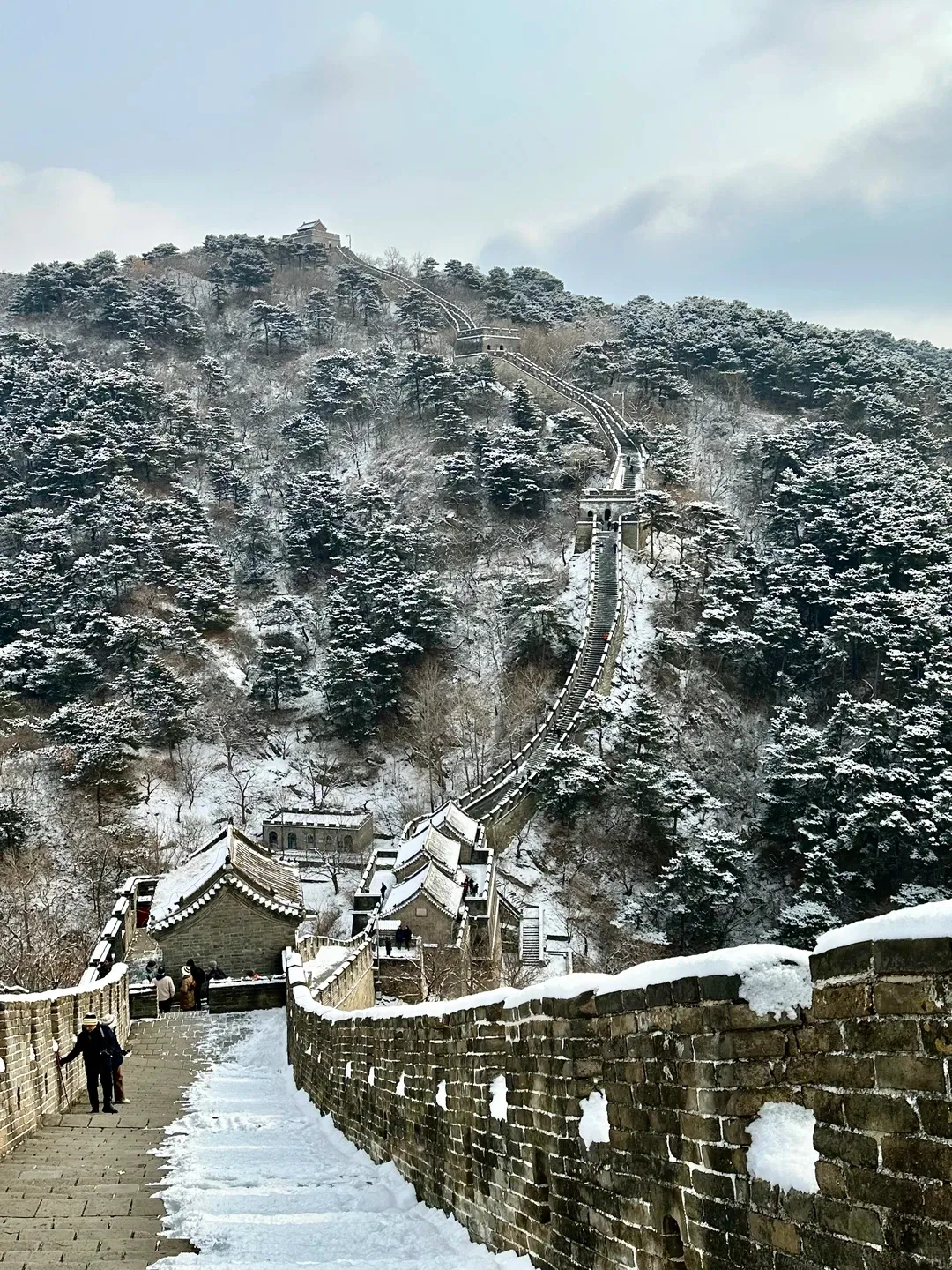 Mutianyu Great Wall climbing a snow-covered ridge, watchtowers fading into the winter mist