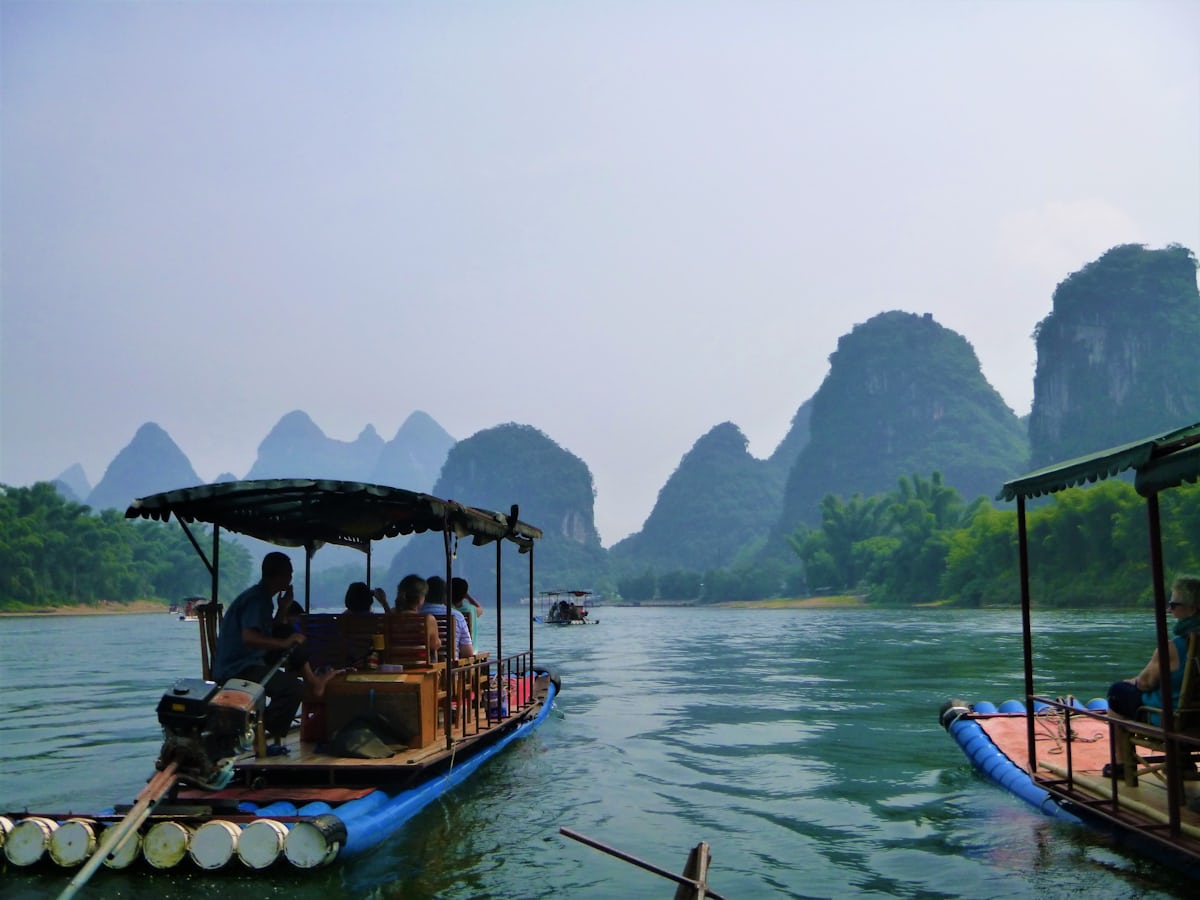 Covered bamboo rafts drift beneath karst peaks — the Yulong River rides are quieter than the main Li River cruise