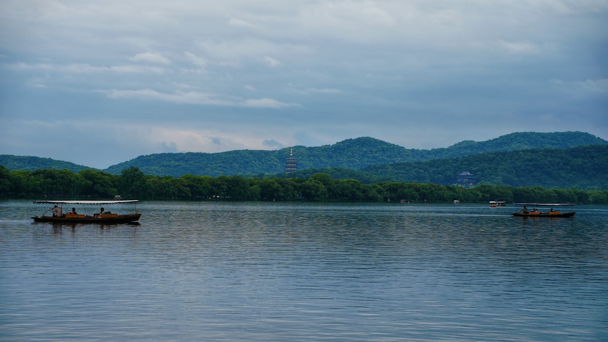 Wooden boats drift on West Lake with Leifeng Pagoda on the south shore — top-floor views peak in the hour before sunset