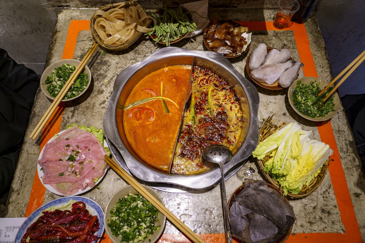A yuanyang hotpot from above — red mala broth on one side, mild on the other, plates ready to drop in